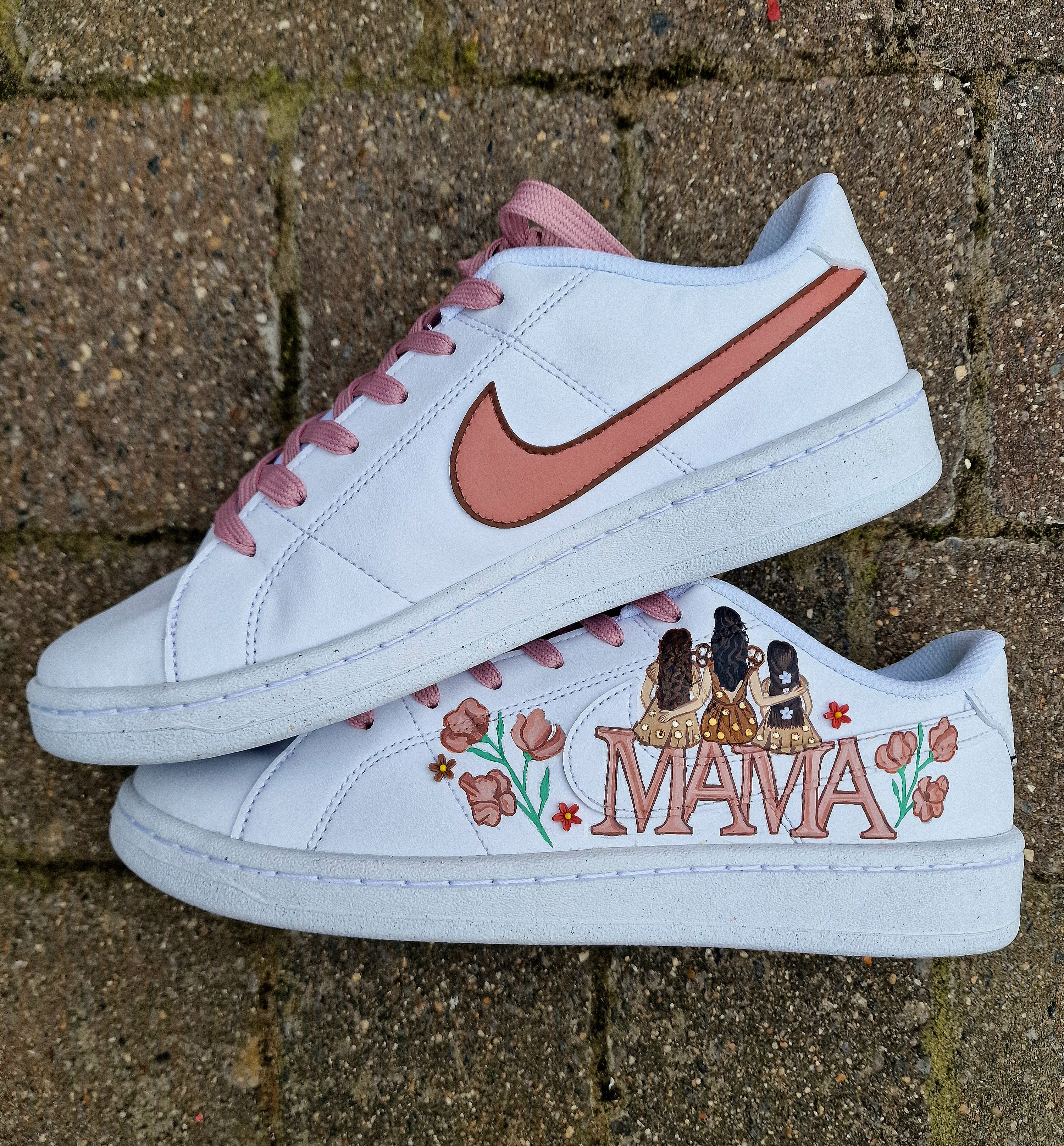 Custom hand-painted Nike sneakers featuring a realistic portrait of a mother and her daughters, personalized names, floral details, and loving elements like “Mama” and “Ba.” Crafted in white leather with pink swooshes and laces, these shoes are a perfect Mother’s Day gift showcasing unique wearable art.


