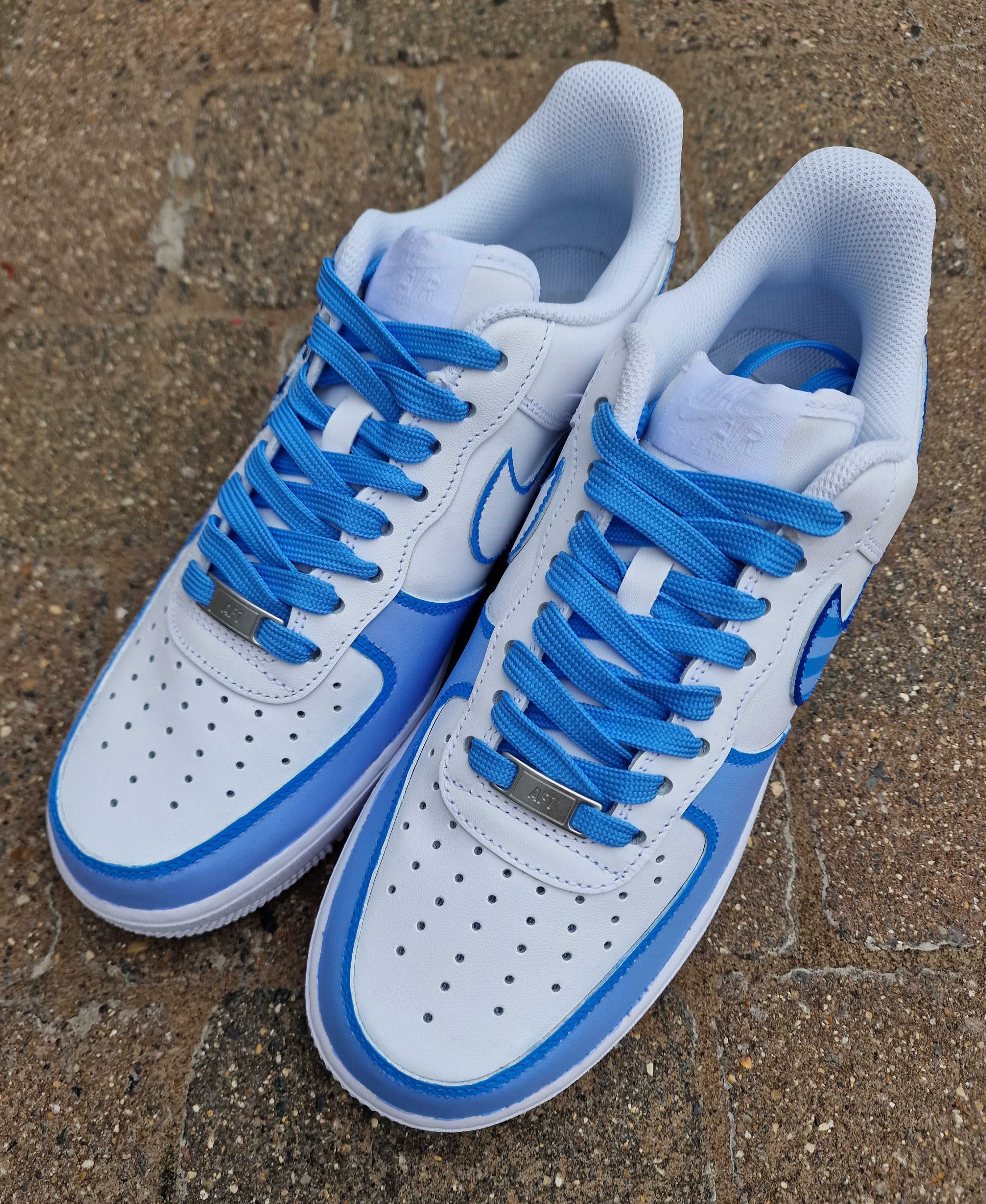 A pair of custom hand-painted Nike Air Force 1 sneakers featuring detailed artwork of the Manchester City Football Club crest, signature blue hues, striped swoosh, and personalized finishing, crafted by Gitartsy for football fans and sneaker collectors.

