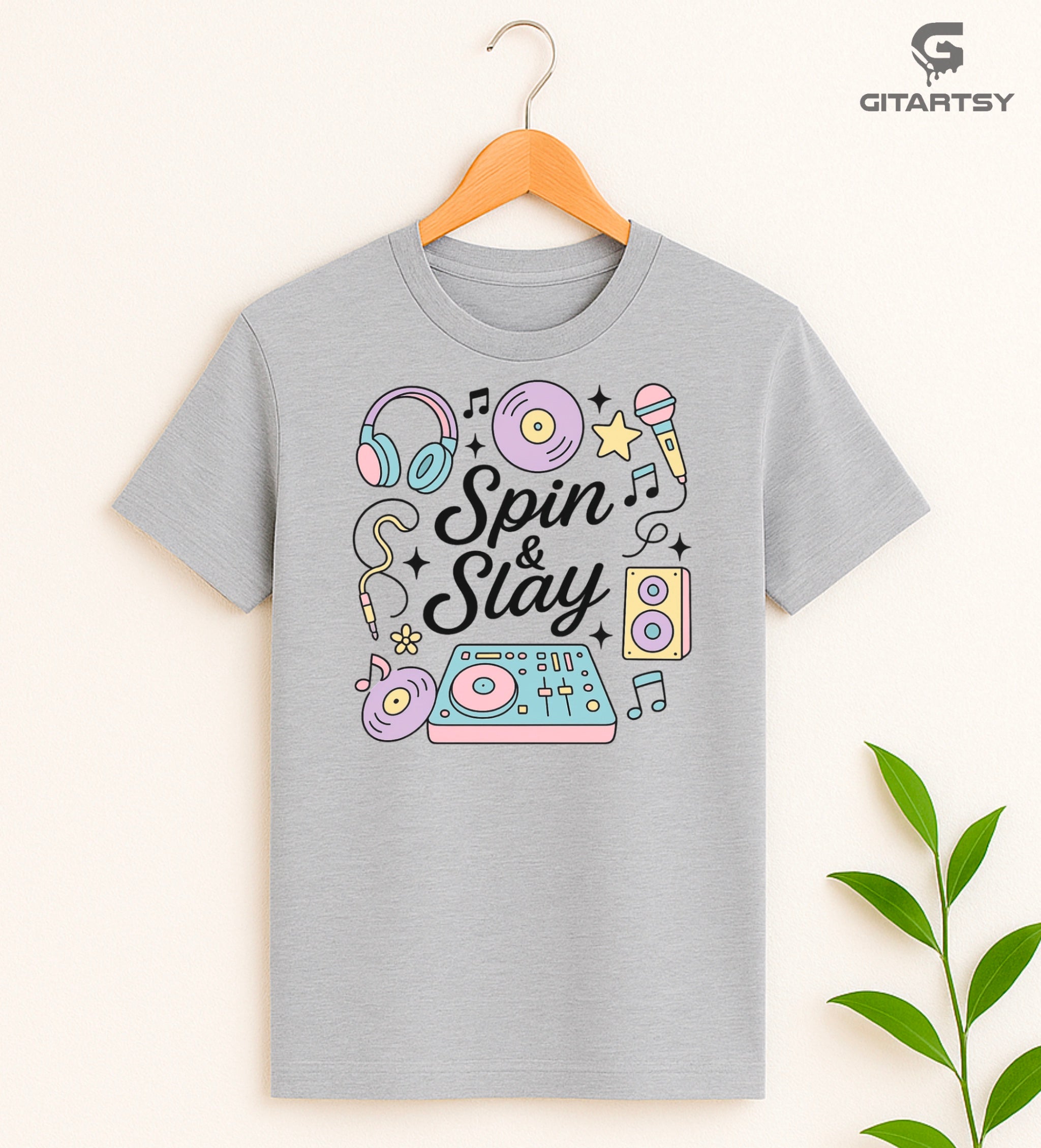 Pastel “Spin & Slay” DJ-themed T-shirt with illustrations of headphones, turntable, vinyl, mic, and speakers – ideal for DJs and music producers.