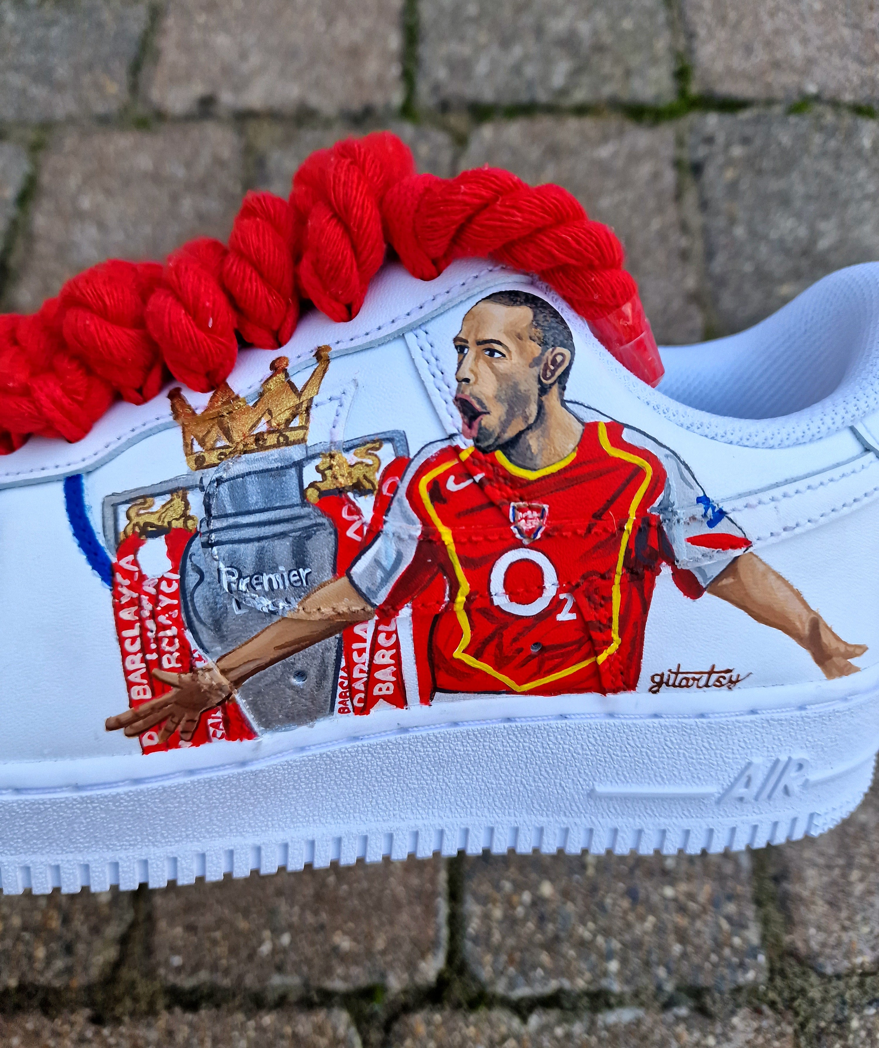 Hand-painted custom Nike Air Force 1 sneakers featuring Arsenal legend Thierry Henry, the Arsenal crest, Premier League trophy, and bold red laces. Perfect for Arsenal fans and football sneaker collectors.

