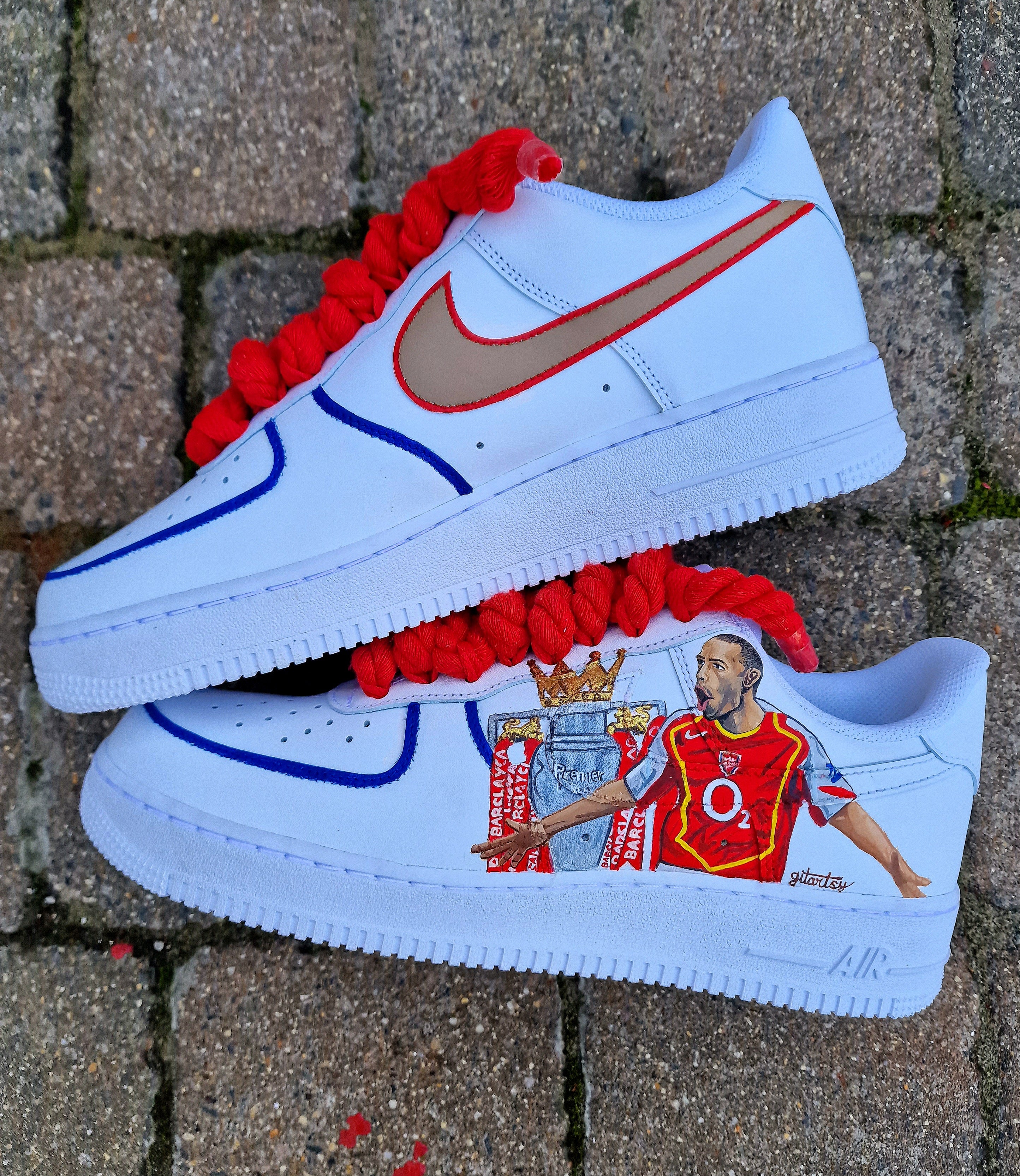 Hand-painted custom Nike Air Force 1 sneakers featuring Arsenal legend Thierry Henry, the Arsenal crest, Premier League trophy, and bold red laces. Perfect for Arsenal fans and football sneaker collectors.

