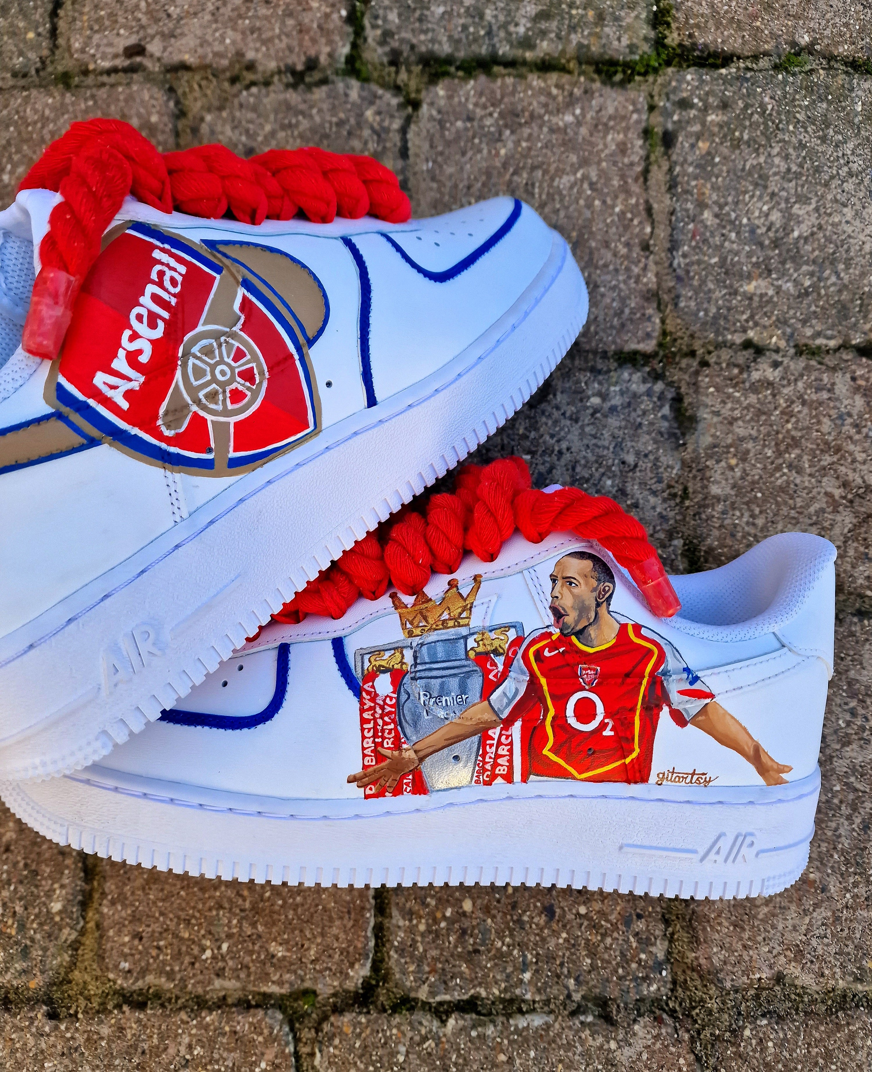 Hand-painted custom Nike Air Force 1 sneakers featuring Arsenal legend Thierry Henry, the Arsenal crest, Premier League trophy, and bold red laces. Perfect for Arsenal fans and football sneaker collectors.

