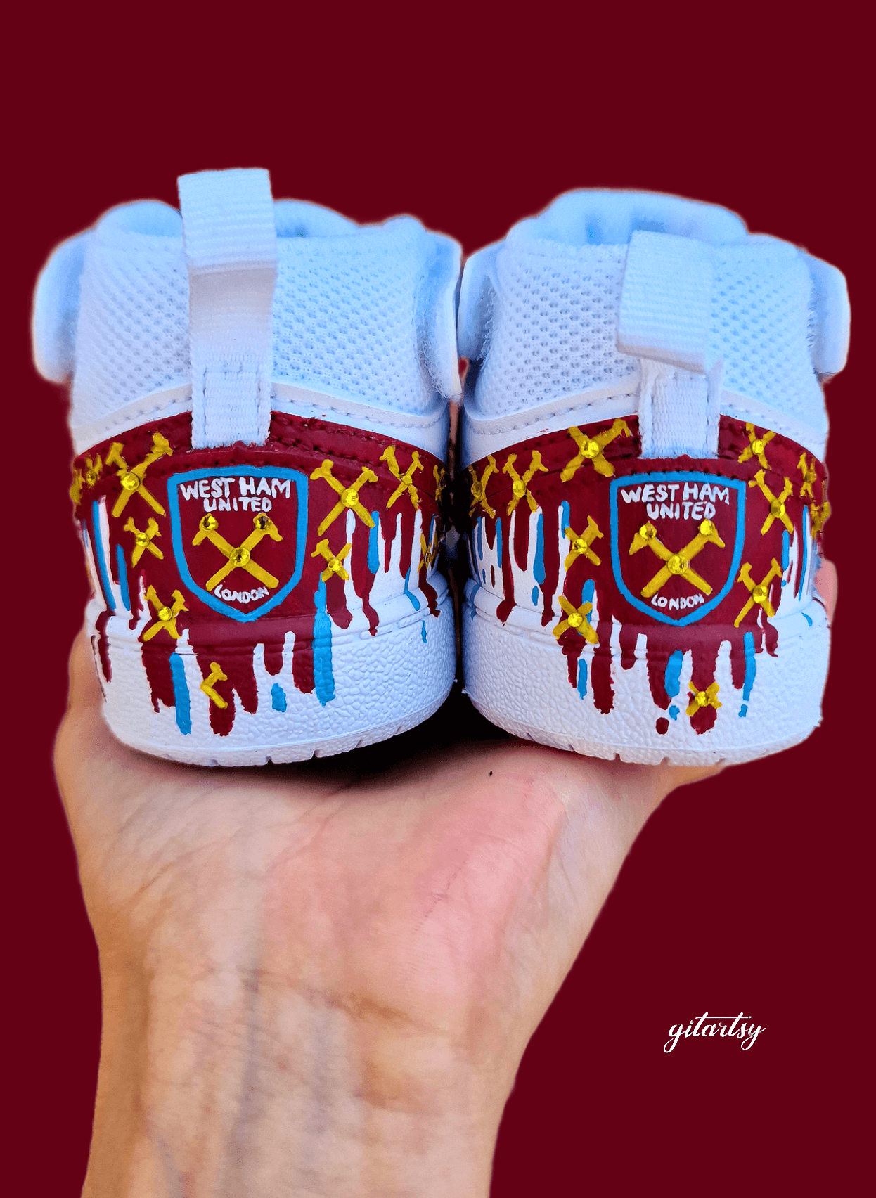 Custom hand-painted baby sneakers inspired by West Ham United, featuring claret and blue color detailing, dripping paint effect, crossed hammers, and personalised names or messages on the straps. Perfect for infant football fans and thoughtful baby gifts.

